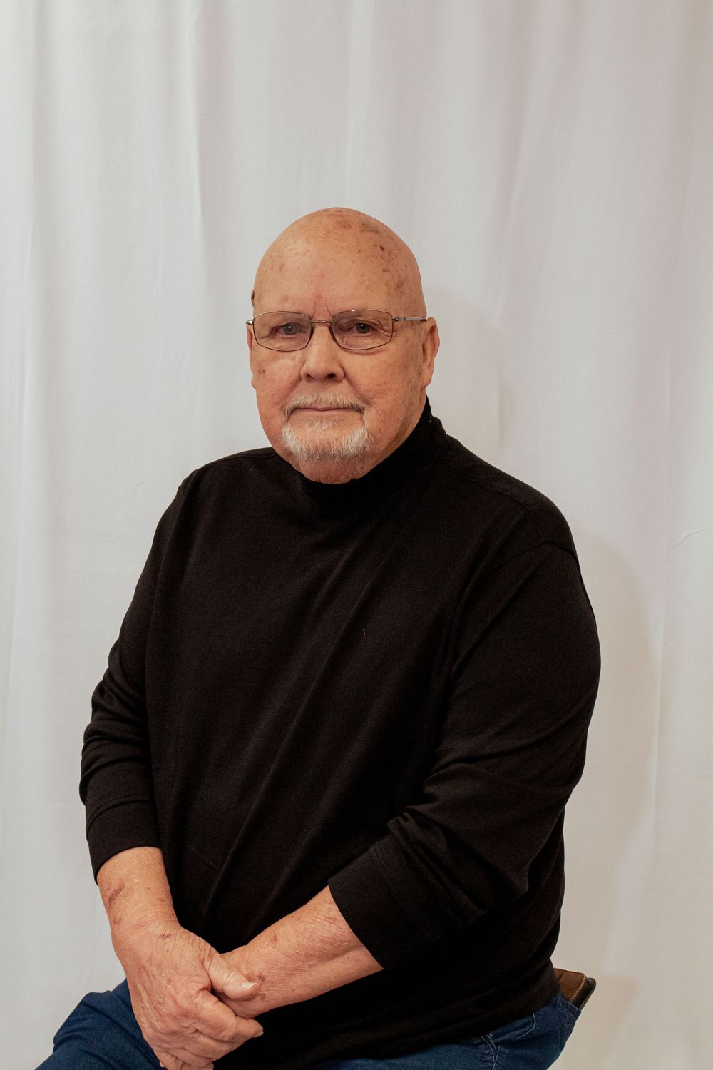 Professional portrait against white backdrop featuring person in black turtleneck sweater and glasses.