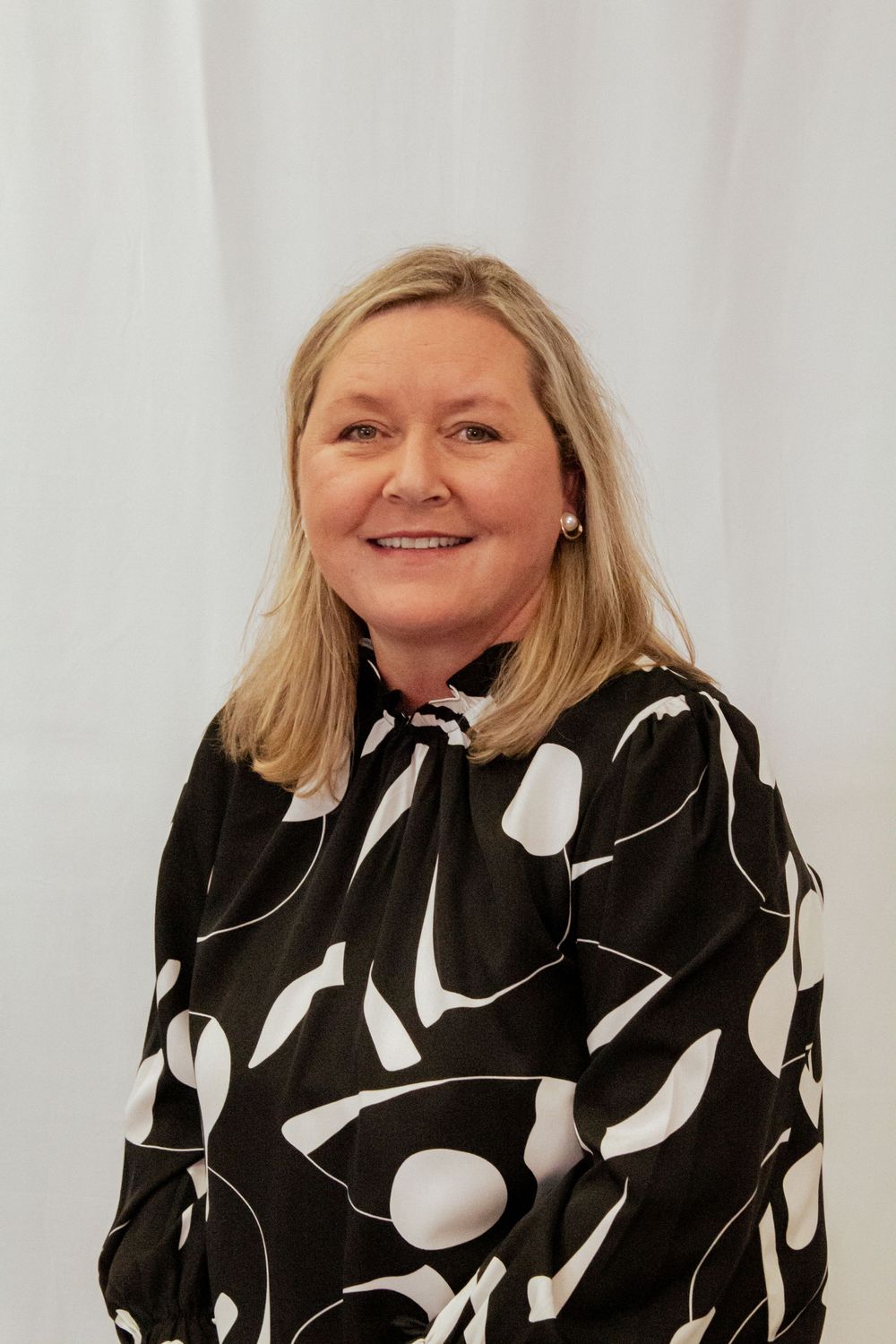 Professional portrait against white backdrop featuring person in bold black and white patterned long sleeve blouse.