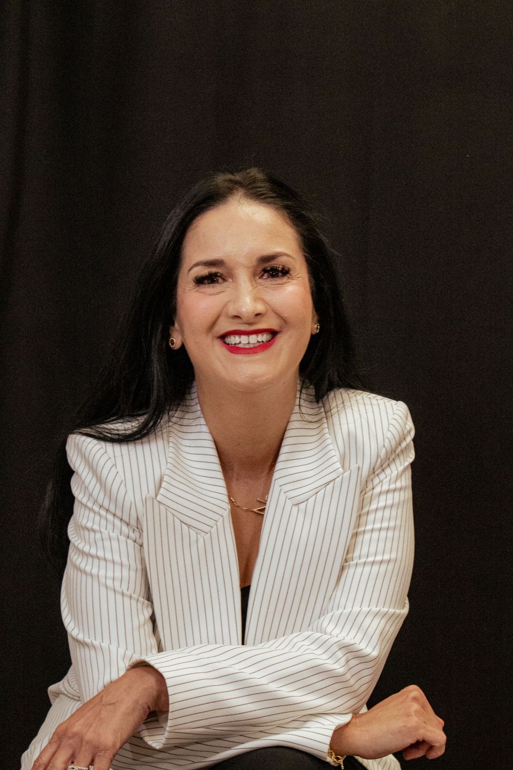 Professional portrait showing a person in a white pinstriped blazer against a dark background.