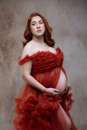 Artistic maternity portrait series featuring a deep red tulle gown against a textured gray backdrop.