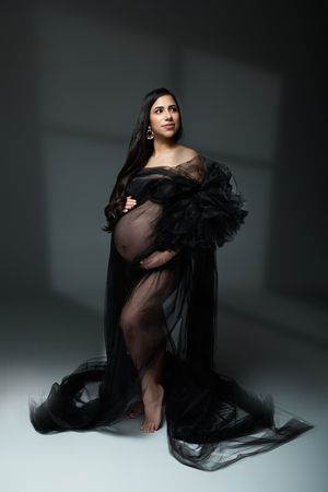 Dramatic maternity portrait with flowing black tulle gown in moody studio lighting.