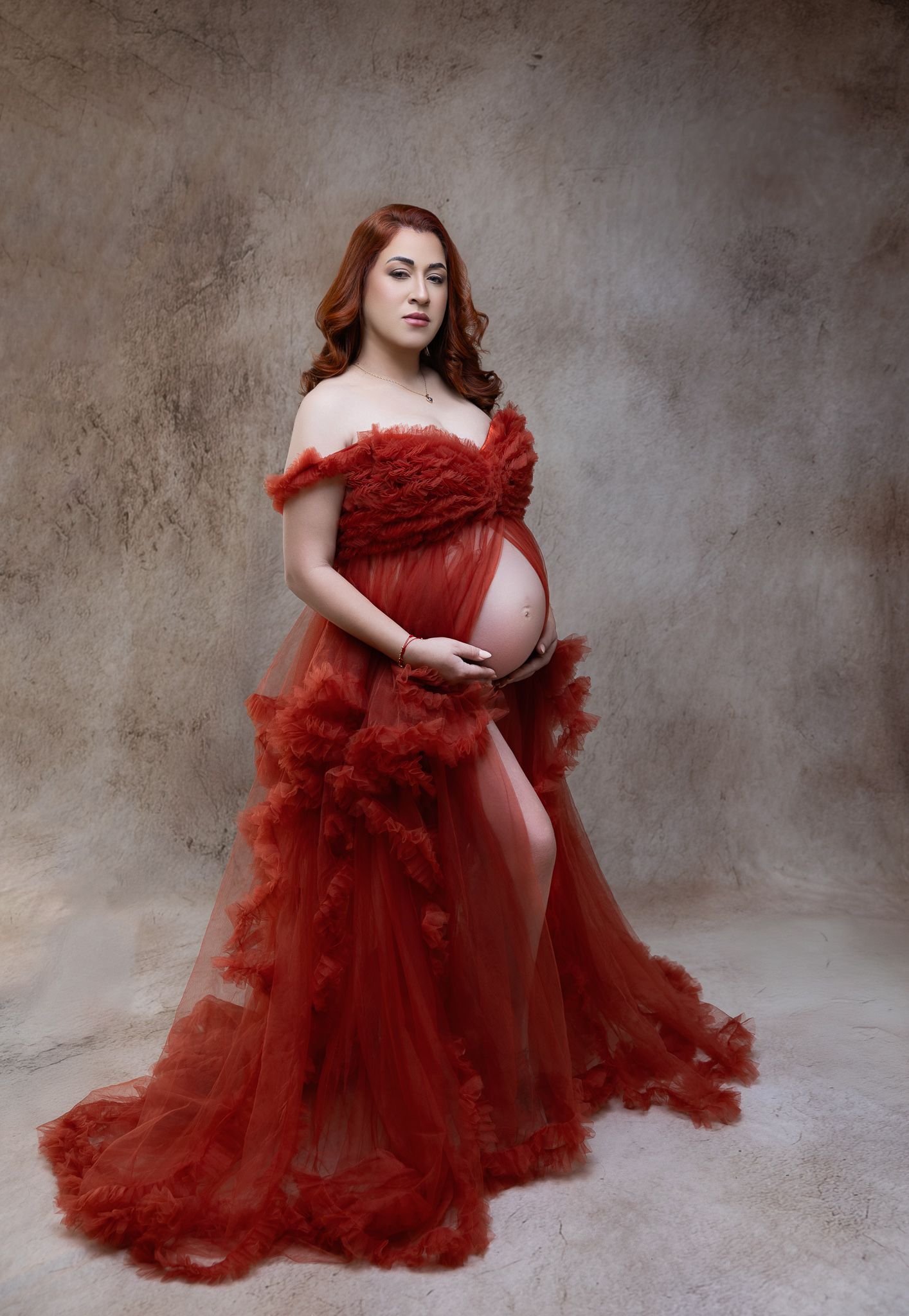 A figure in a flowing deep red tulle gown poses gracefully against a textured gray backdrop in a series of artistic shots.