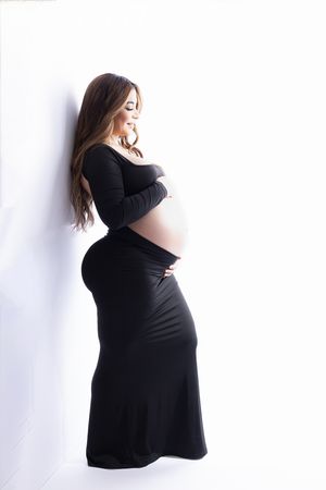 Simple maternity portraits in black dress against white background showing pregnancy silhouette.