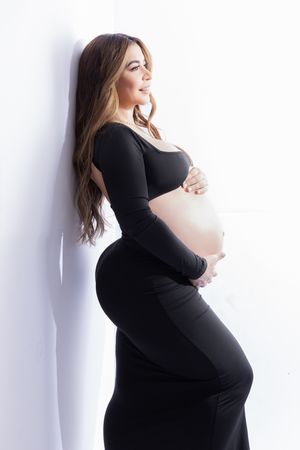Elegant maternity photos showing expectant mother in black dress against white backdrop.