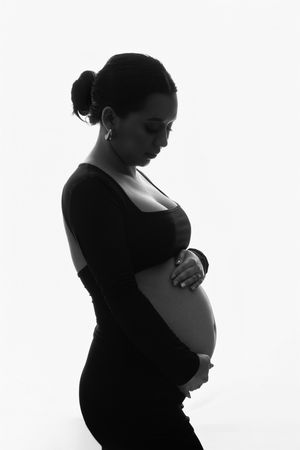 An artistic black and white silhouette portrait of an expectant mother in a form-fitting dress against a white background.