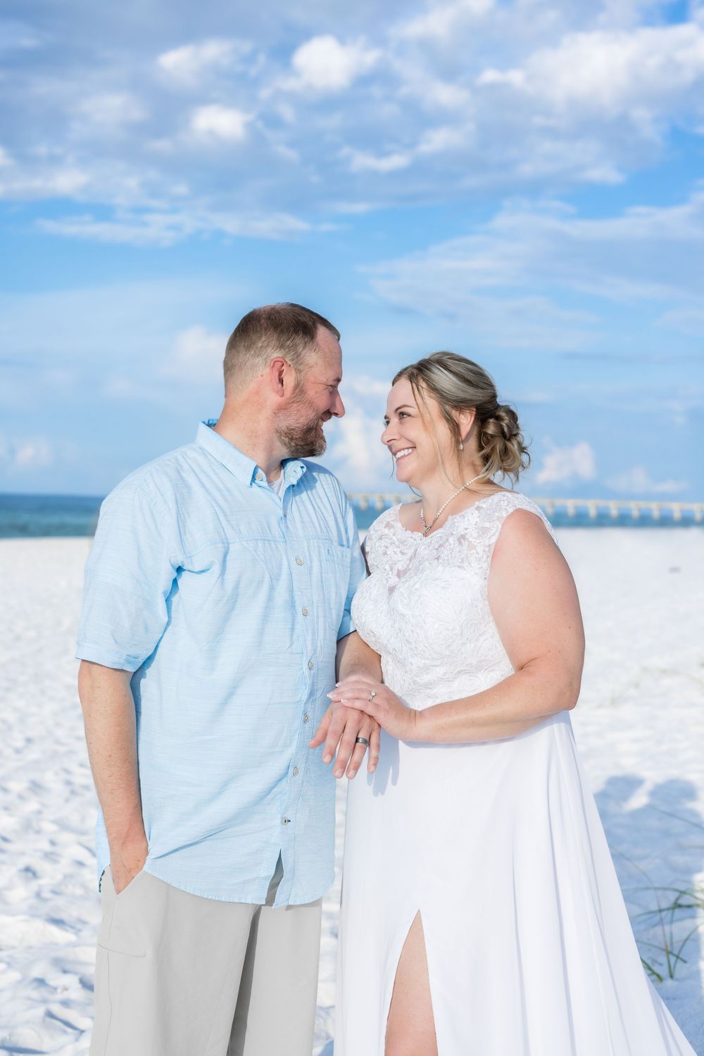 A happy couple shares a joyful moment together on a white sandy beach with blue skies and ocean in the background.