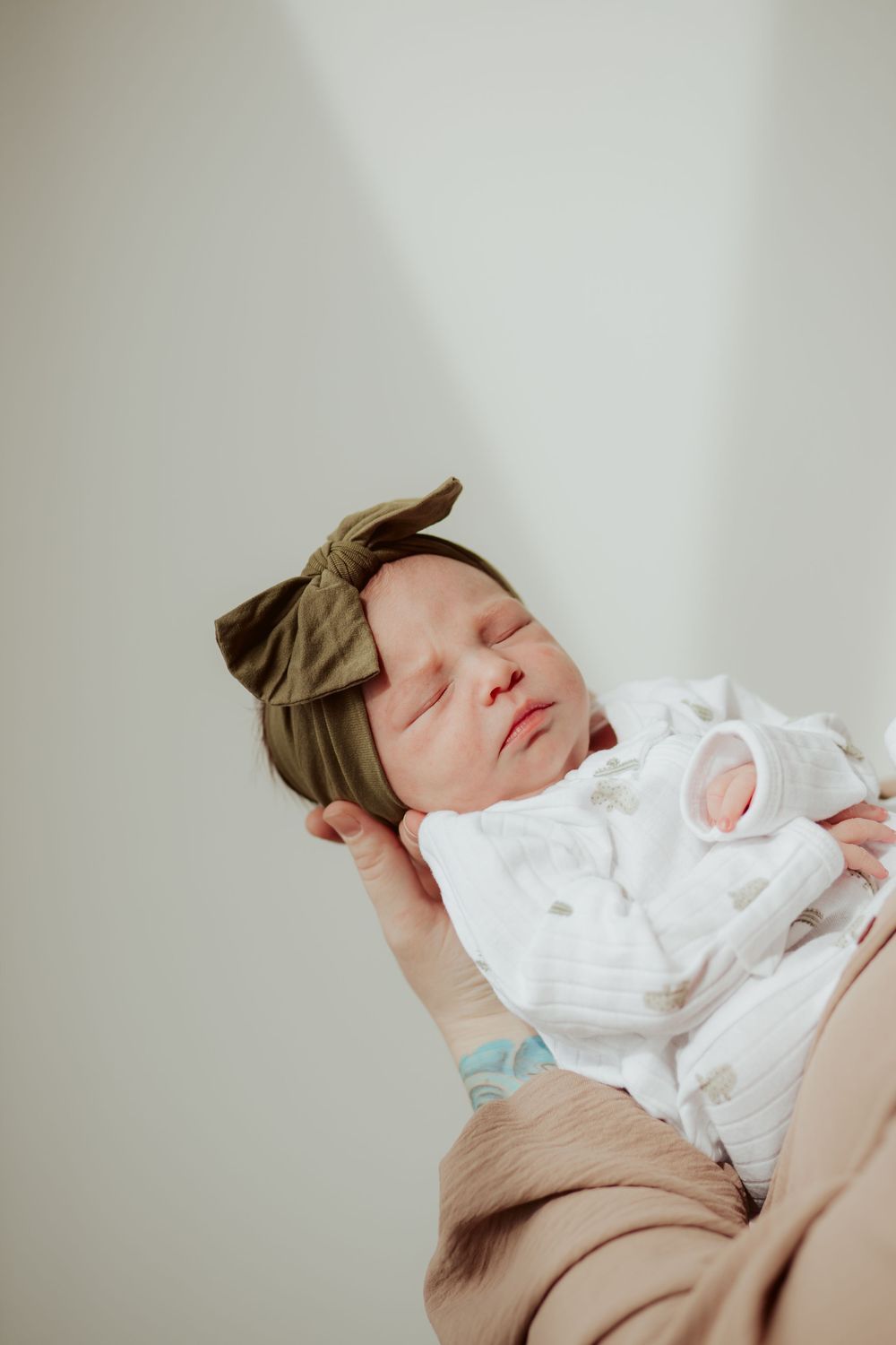 A sleeping infant in a white dress rests peacefully against a soft brown blanket.