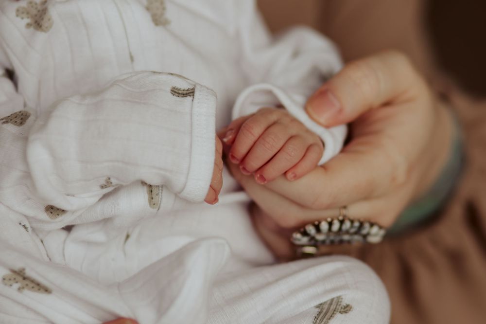 Tiny newborn baby's hand grasps gently against soft white fabric and blanket in tender close-up shot.