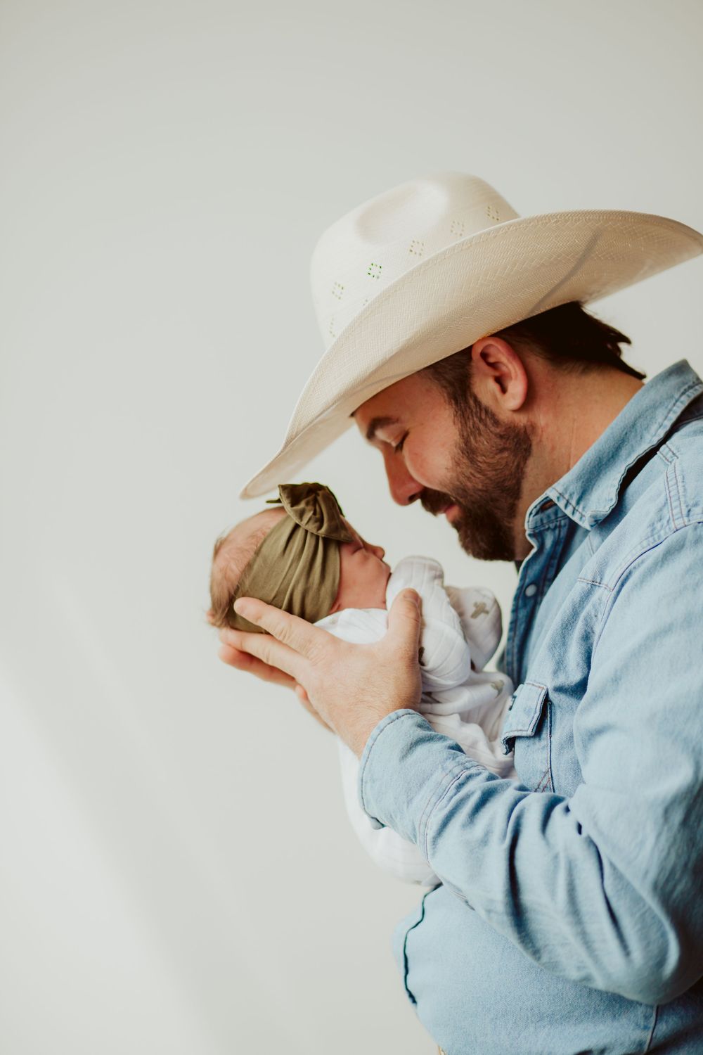 Man in denim shirt and white cowboy hat embraces while connecting emotionally in studio sequence.