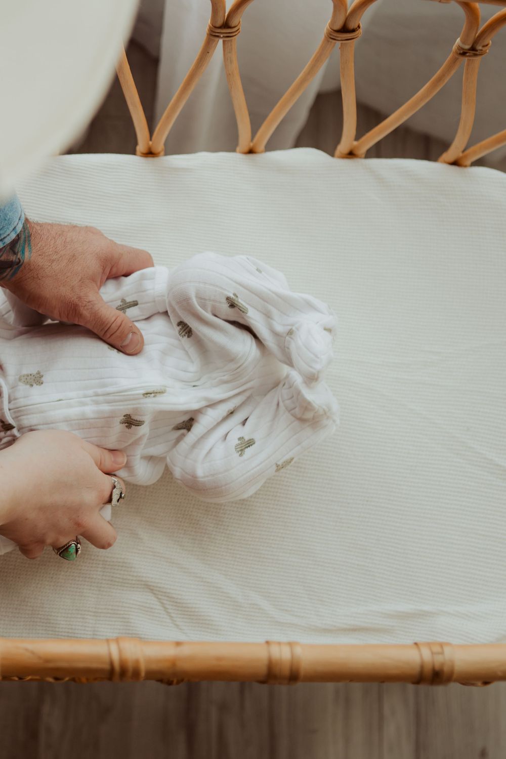 Hands wringing a white fabric or towel on a bamboo chair with a cream-colored cushion.