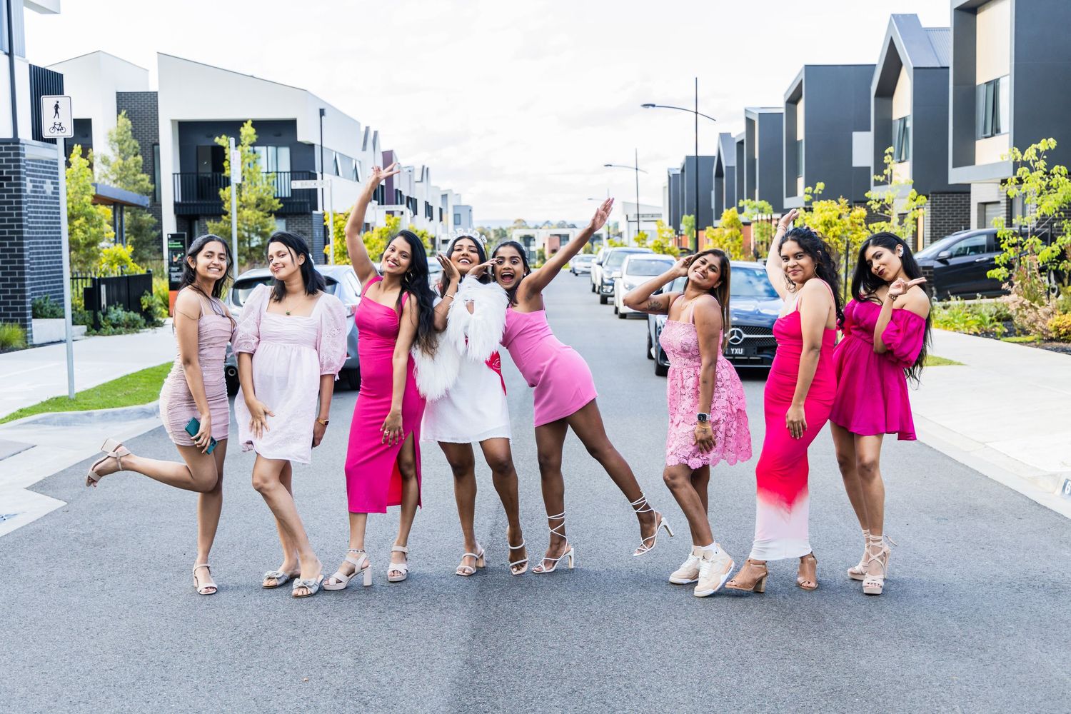 People in pink and white dresses celebrating outdoors at a festive gathering with a residential building in the background.
