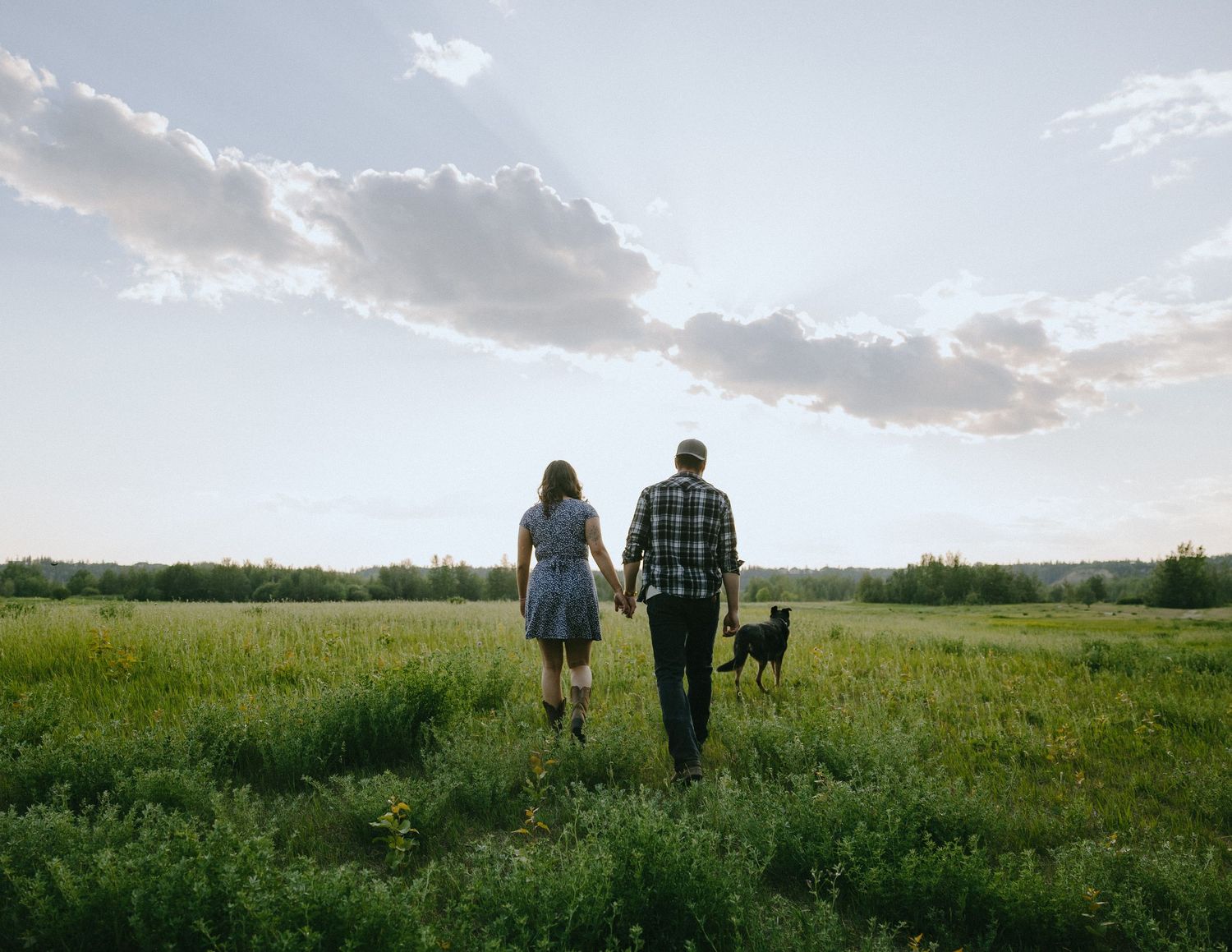 People walking through a scenic green field at sunset with dramatic clouds in the sky.