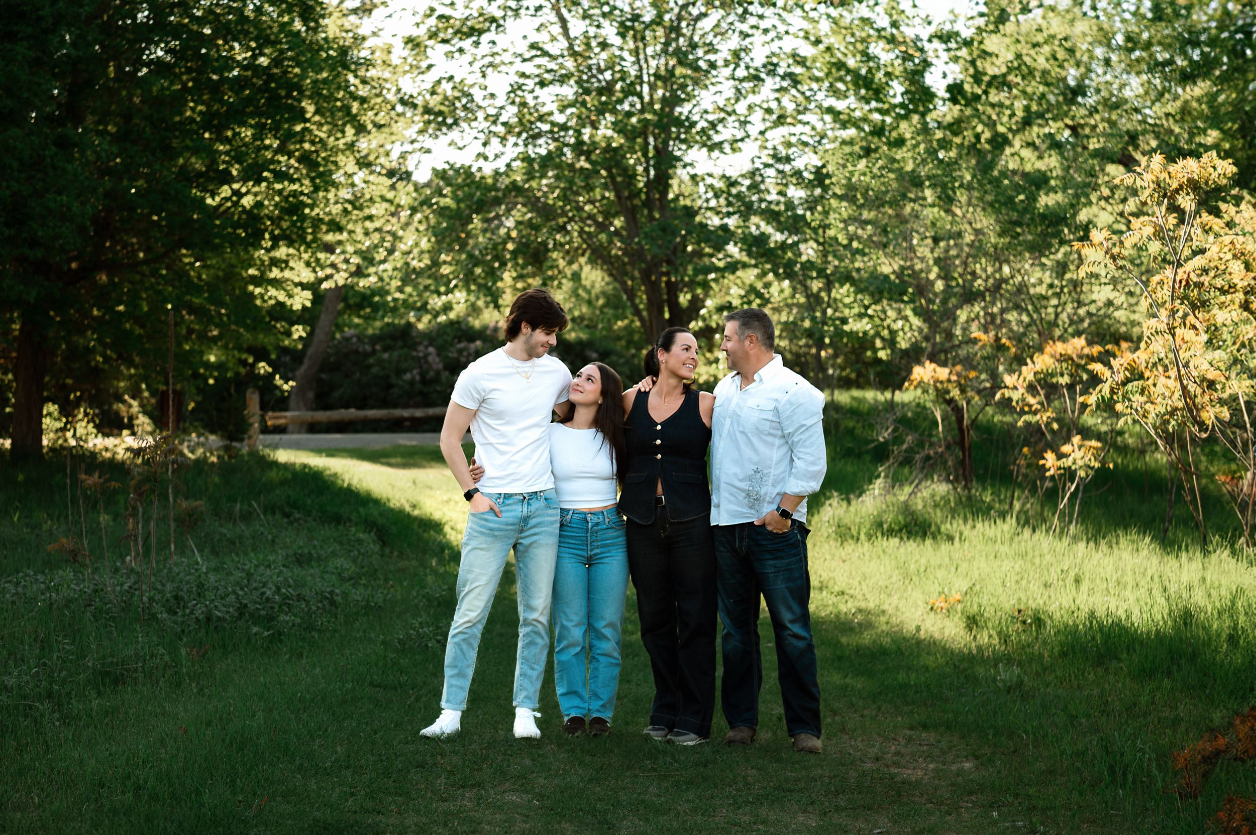 A group stands together outdoors on a grassy path surrounded by green trees on a sunny day.