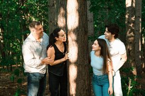 A candid moment of five friends laughing and chatting together in a wooded forest setting.