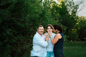 Three people share a joyful moment together outdoors against a lush green backdrop at sunset.