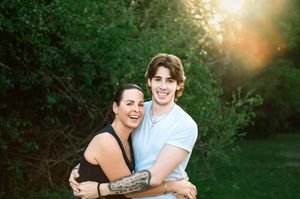 A couple sharing a tender moment in a sunlit garden with green foliage in the background.