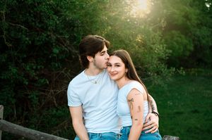 A couple embraces while sitting together outdoors during golden hour with lush greenery in the background.