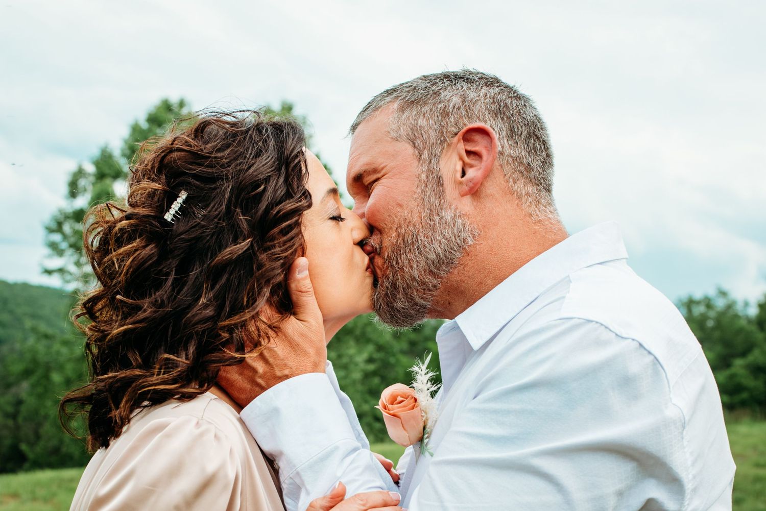 A romantic kiss shared between a bridge and groom in a natural outdoor setting.