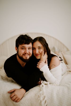 Couple lying together during romantic indoor photoshoot with natural lighting.