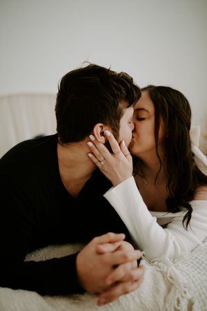 Intimate couple sharing tender kisses against white backdrop in dramatic black and white photography series.