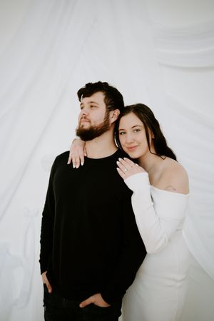 Romantic couple in contrasting black and white outfits pose intimately against white background.