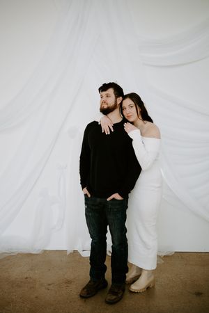 Couple in contrasting outfits share candid moments against minimalist white backdrop.