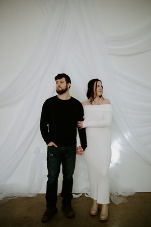 Full-length portrait of couple in black and white outfits against simple studio backdrop.