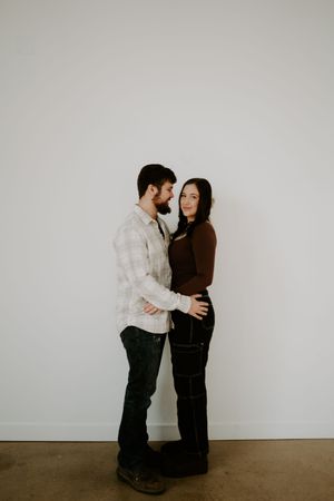 Couple embraces in a minimalist indoor setting against a white wall.