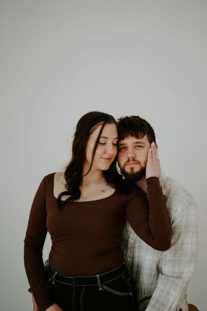 Romantic indoor photoshoot with couple in casual attire against grey background.