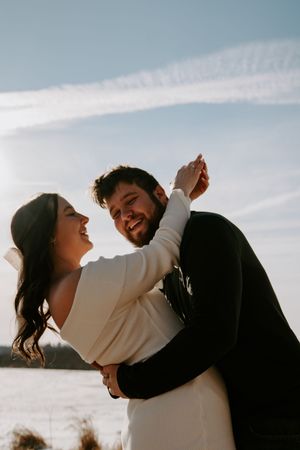 Couple dances and laughs together on beach during golden hour.