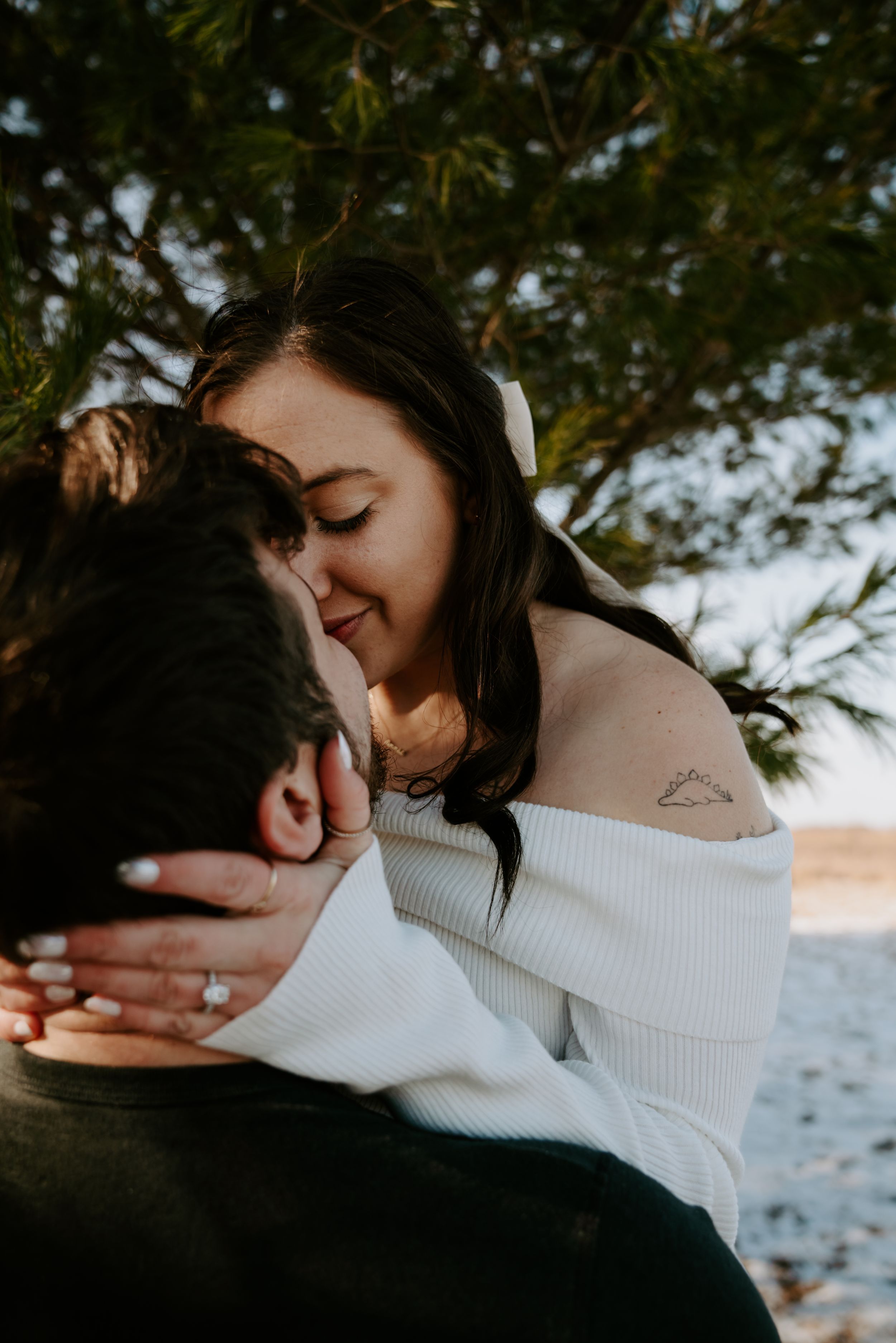 Couple embracing outdoors near water with trees in background.