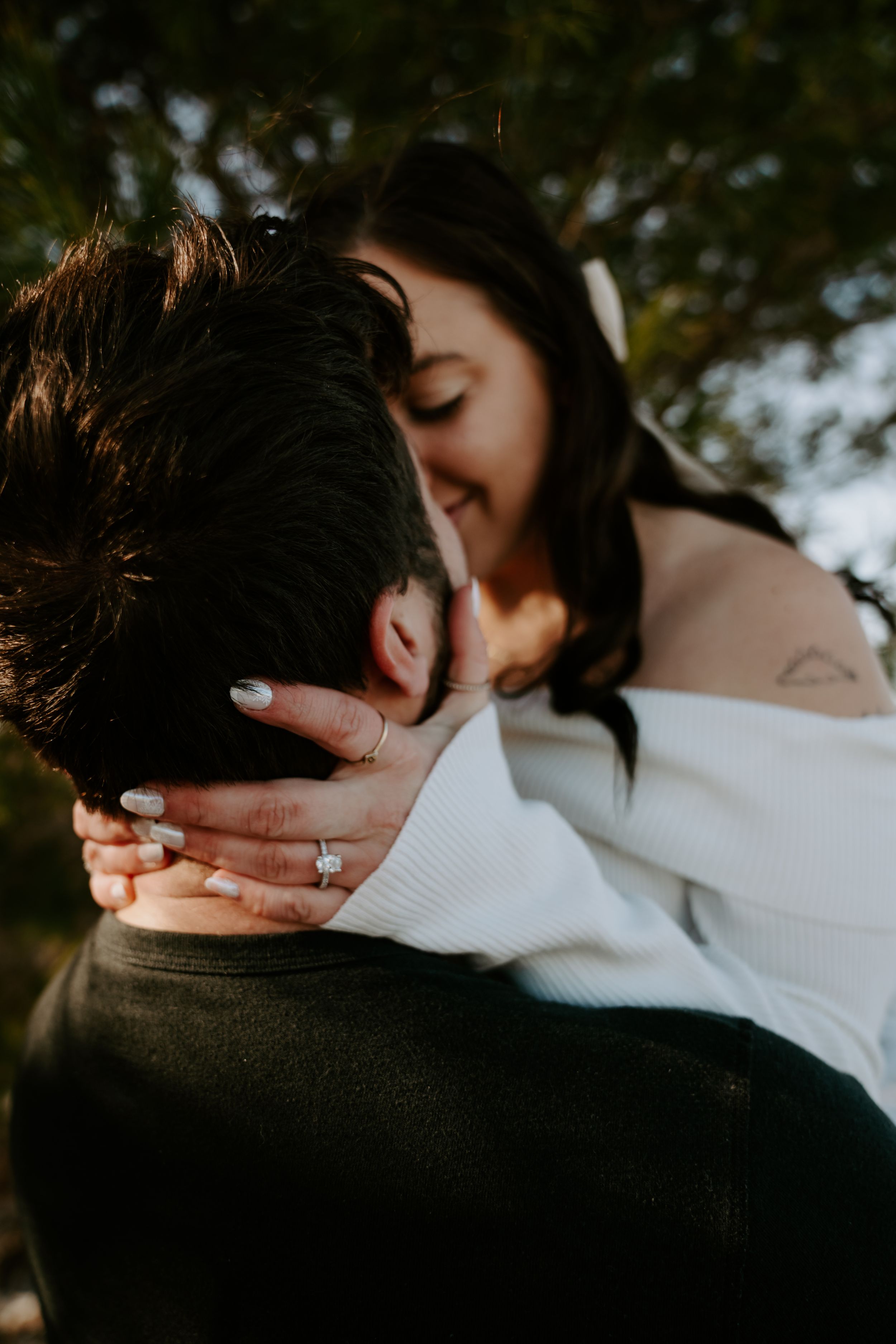 Intimate couple embracing in natural outdoor setting with white sweater and dark clothing visible.