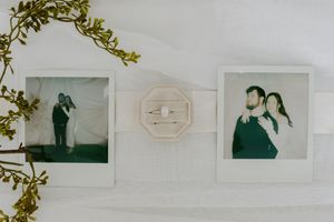 Wedding photos displayed with decorative greenery against a light wall.