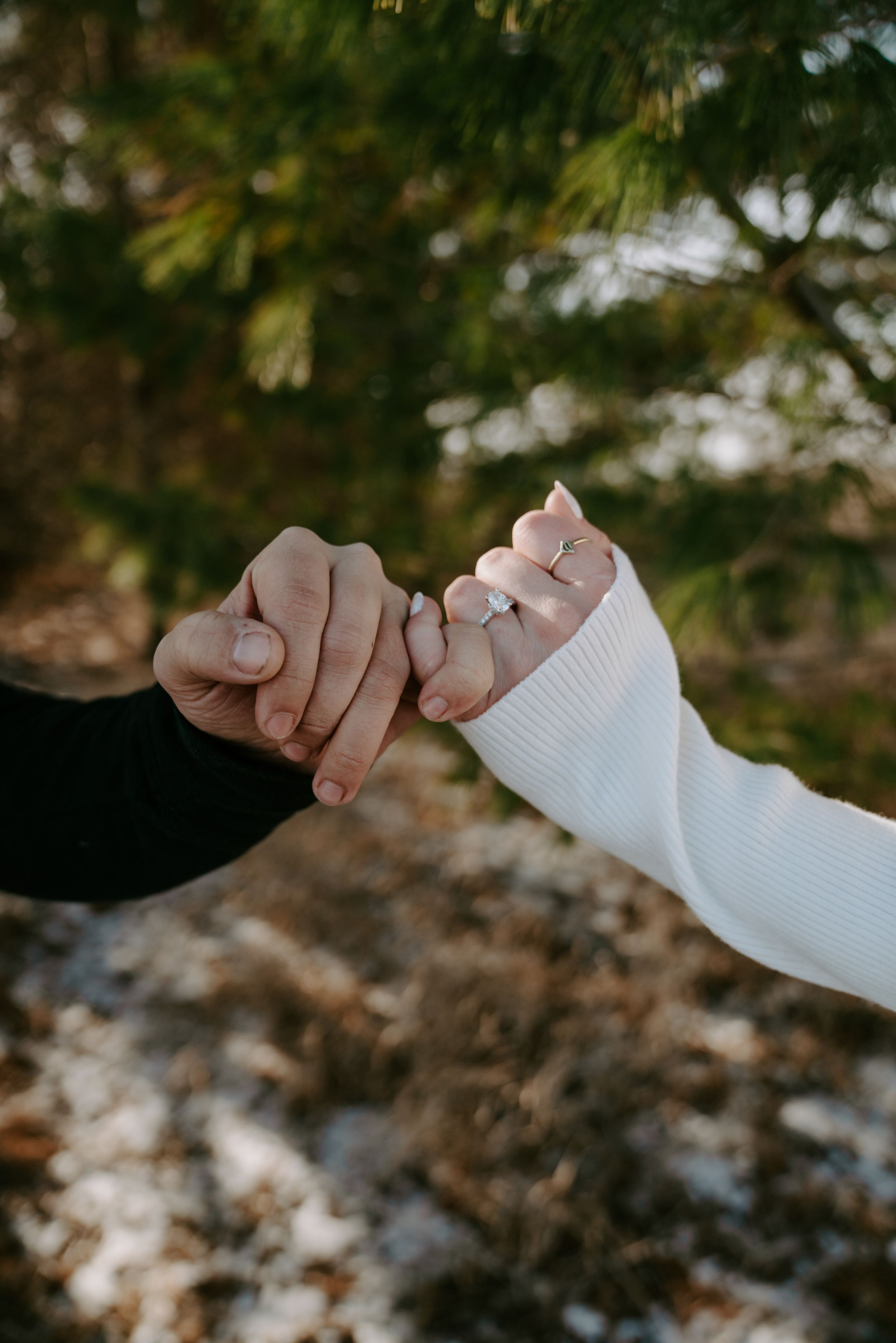 Close-up of intertwined hands with engagement ring against natural background.