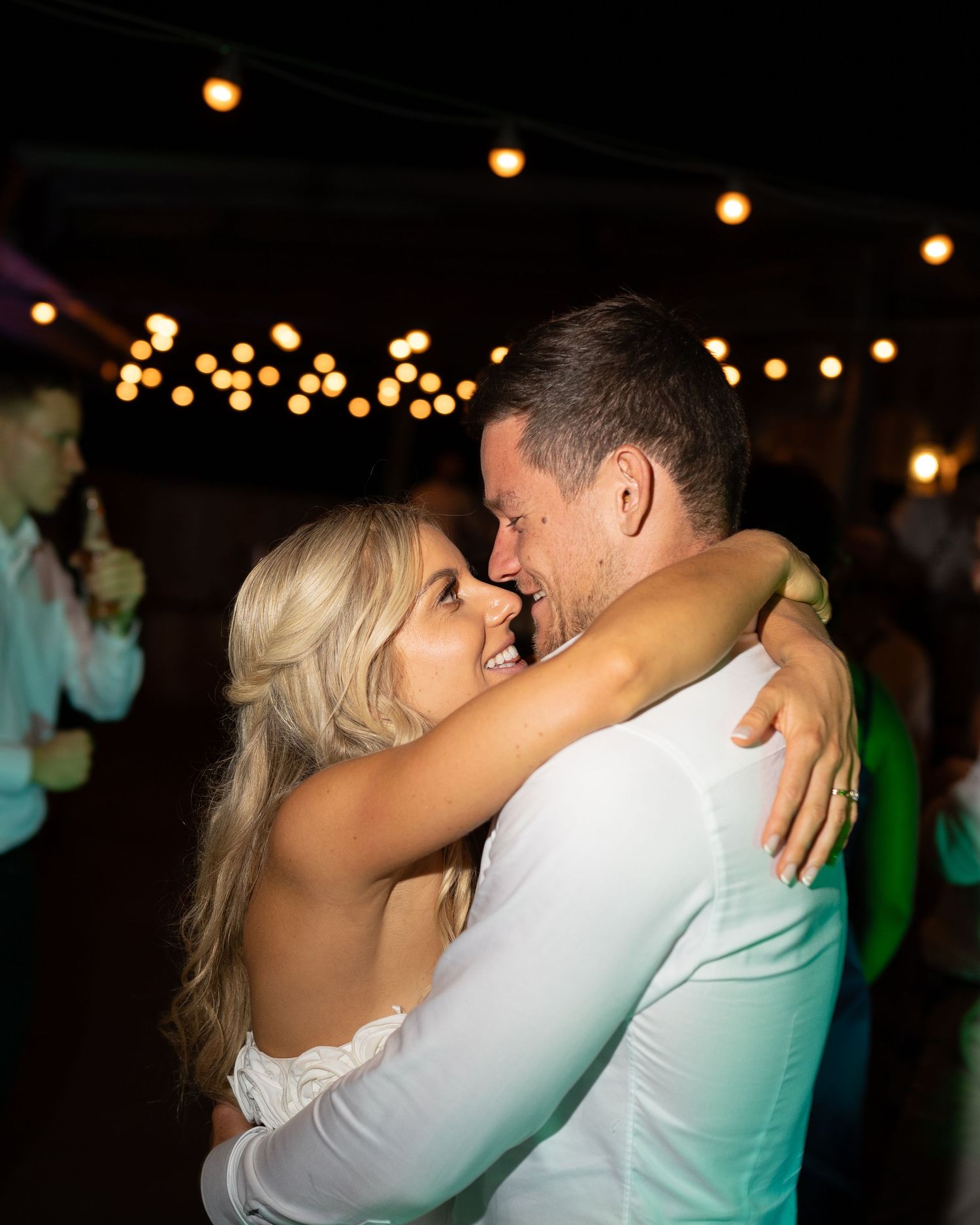 Wedding couple shares a romantic dance under string lights at their evening reception.