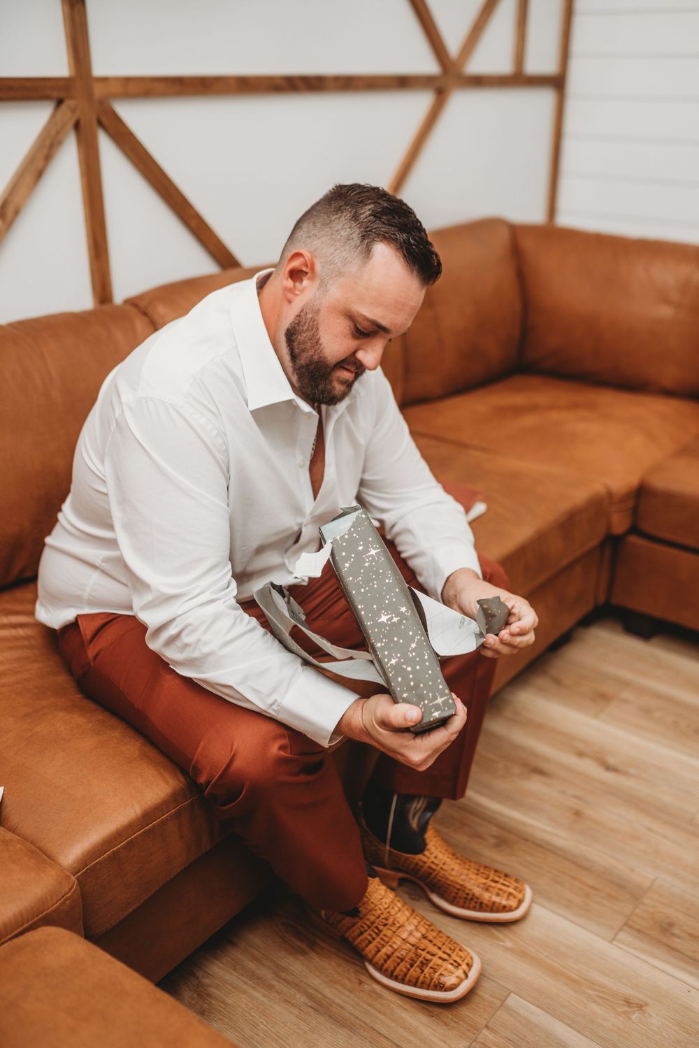 Person in white button-down shirt puts on grey socks while sitting on brown leather couch.
