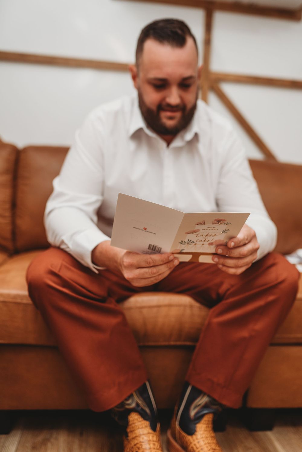 Person on brown leather couch reads greeting cards with joyful expression.
