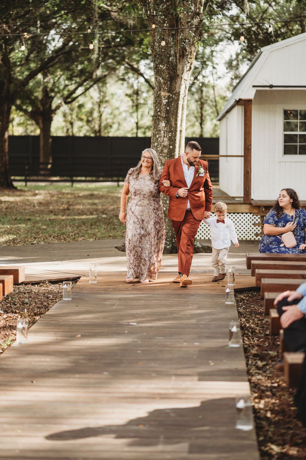 A couple walks with a small child down a wooden pathway during an outdoor wedding ceremony.