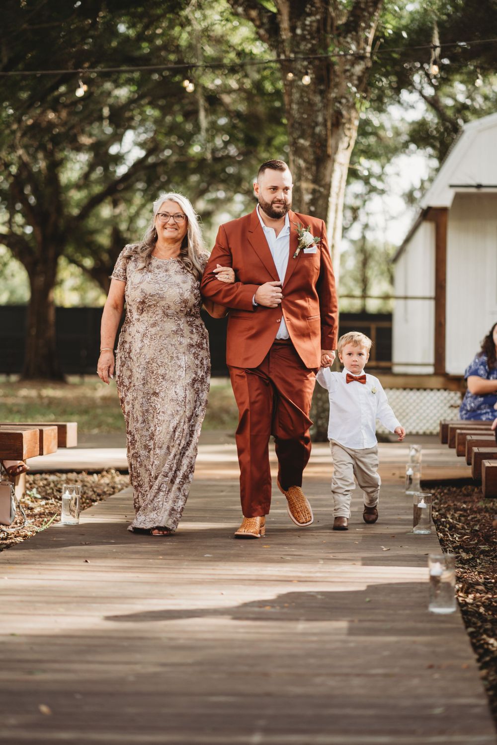 A family walks down a wooden pathway during a wedding ceremony with a young child between them.