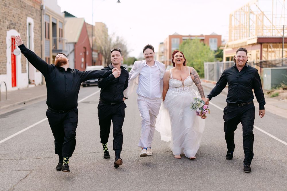 Wedding party walking together down an urban street with industrial buildings in the background.
