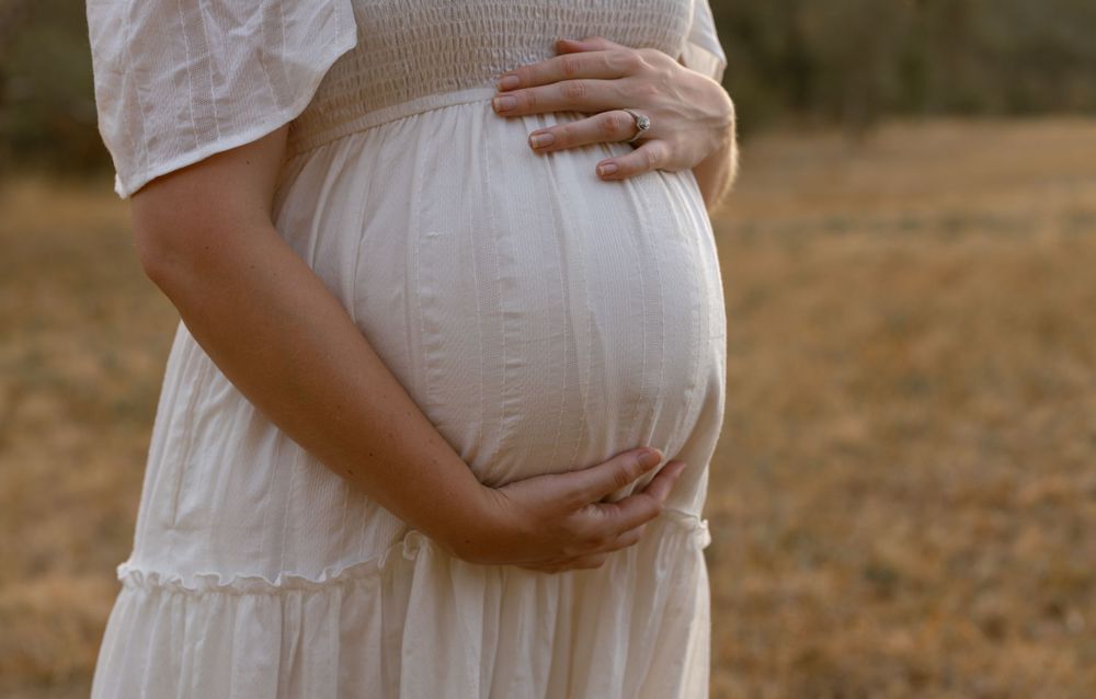 Silhouetted maternity series showing a pregnant woman in white dress against warm sunset light outdoors.