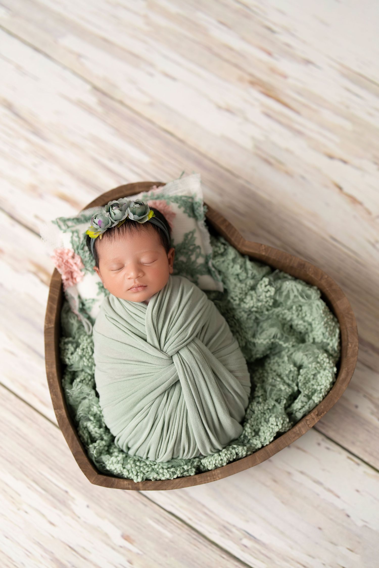 Newborn babygirl wrapped in mint green in a heart shaped bowl