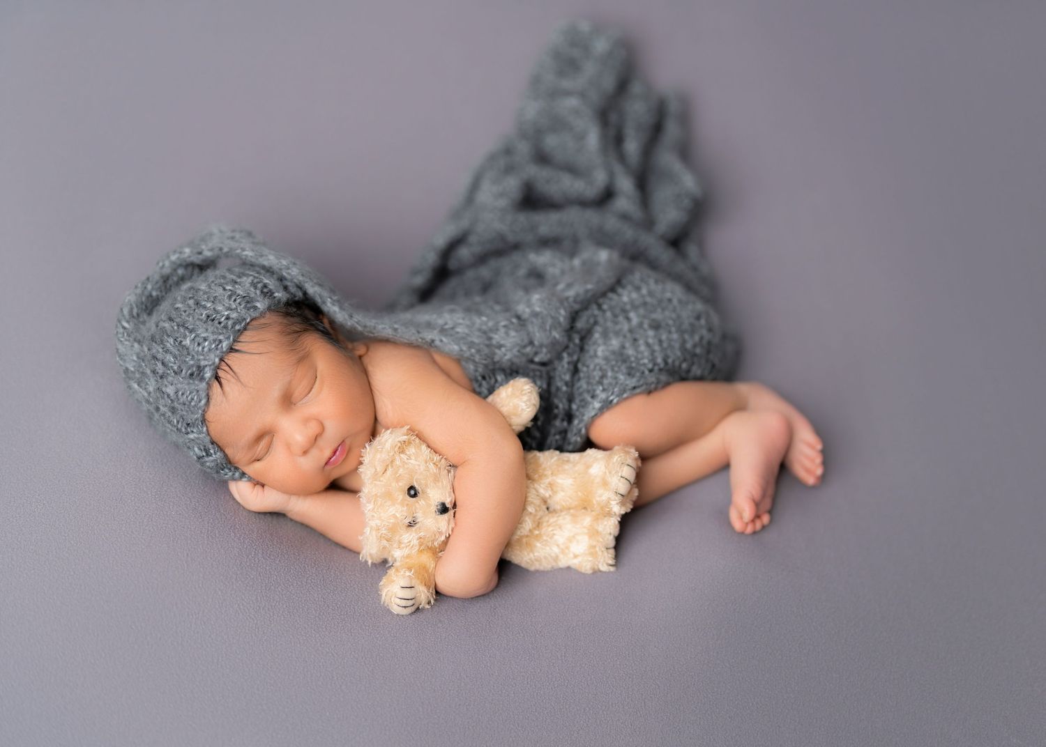 newborn baby boy side with shat laying with a teddy bear in hand