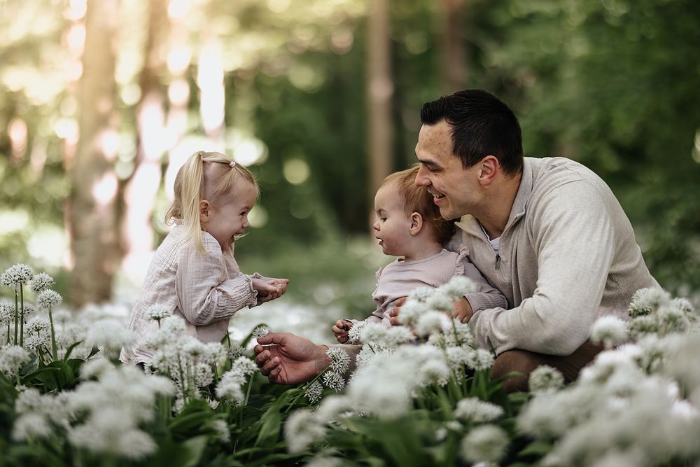 A loving moment shared among family members laying in a field of white flowers in a sunlit forest setting.