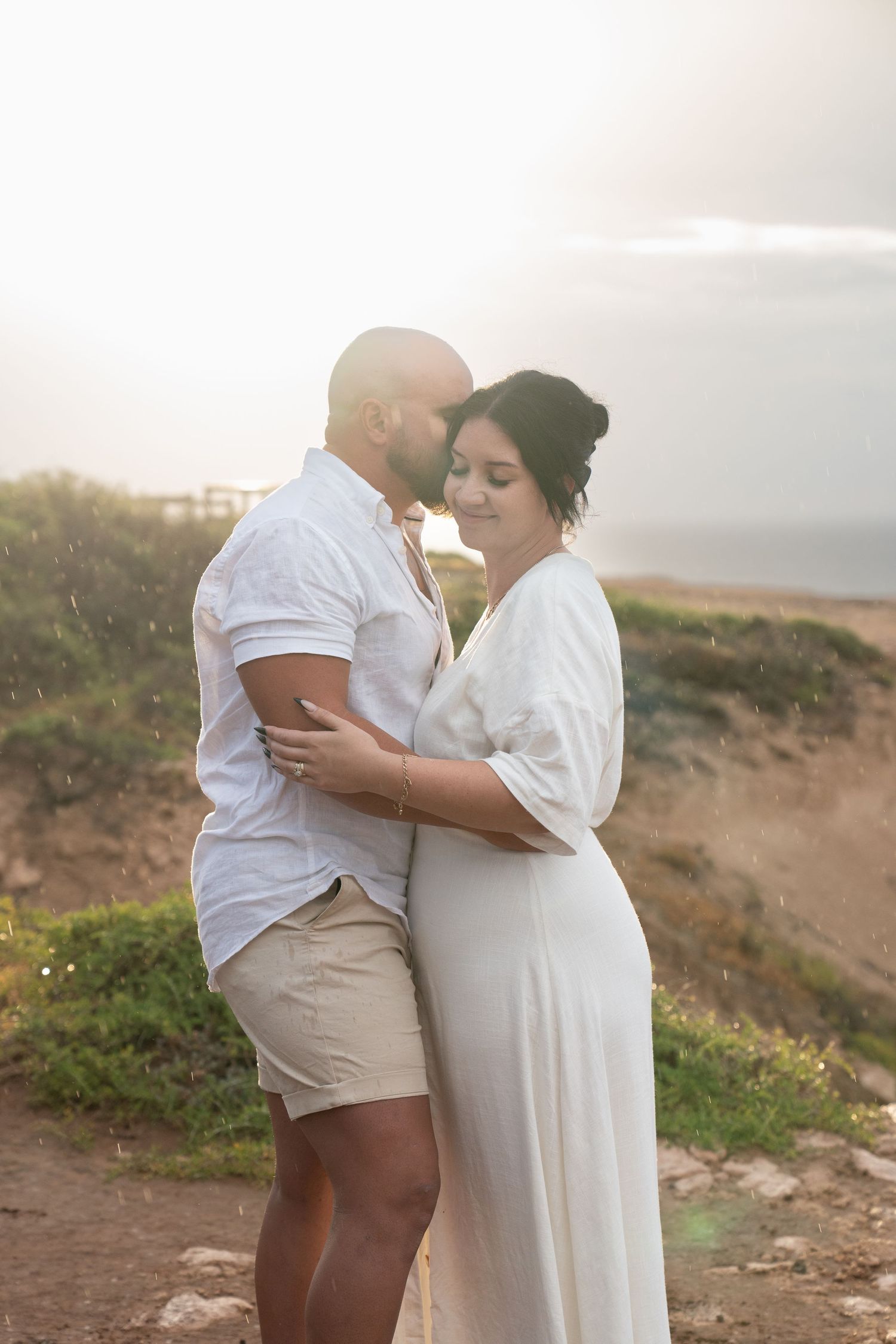 Intimate couple shares a tender moment on a hilltop during golden hour.