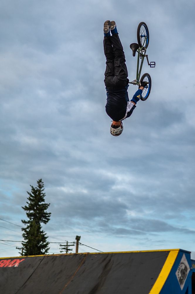 BMX rider performs inverted aerial trick against cloudy sky.