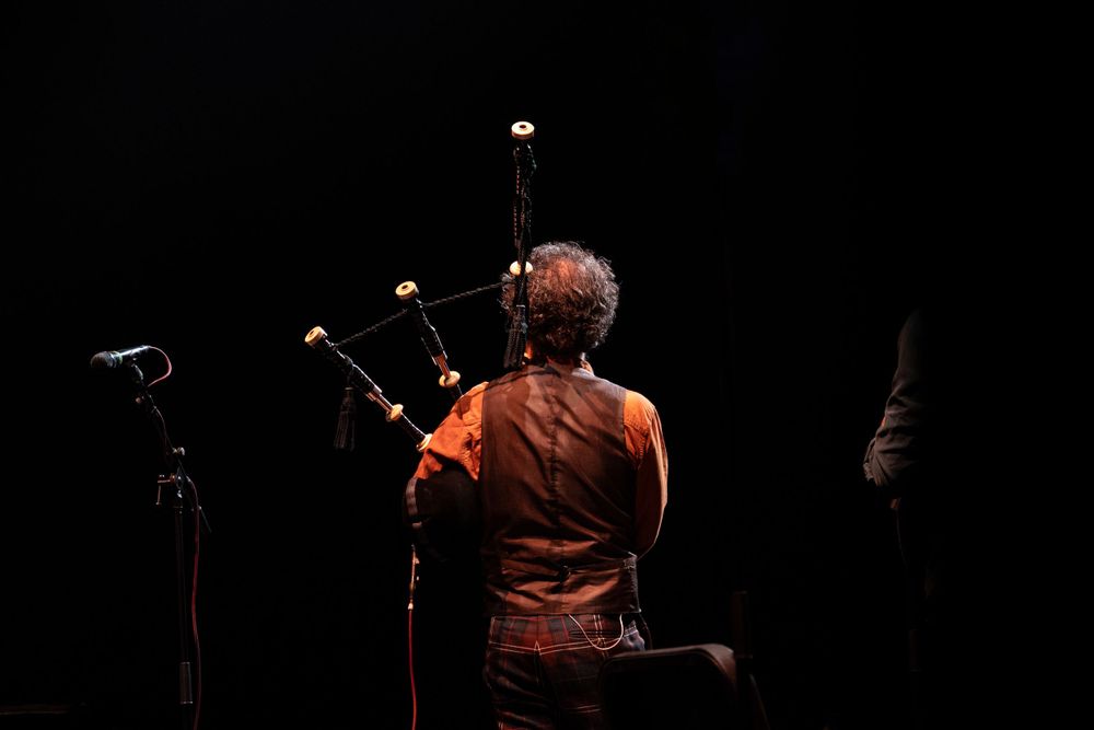 Back view of performer playing bagpipes on dark stage.