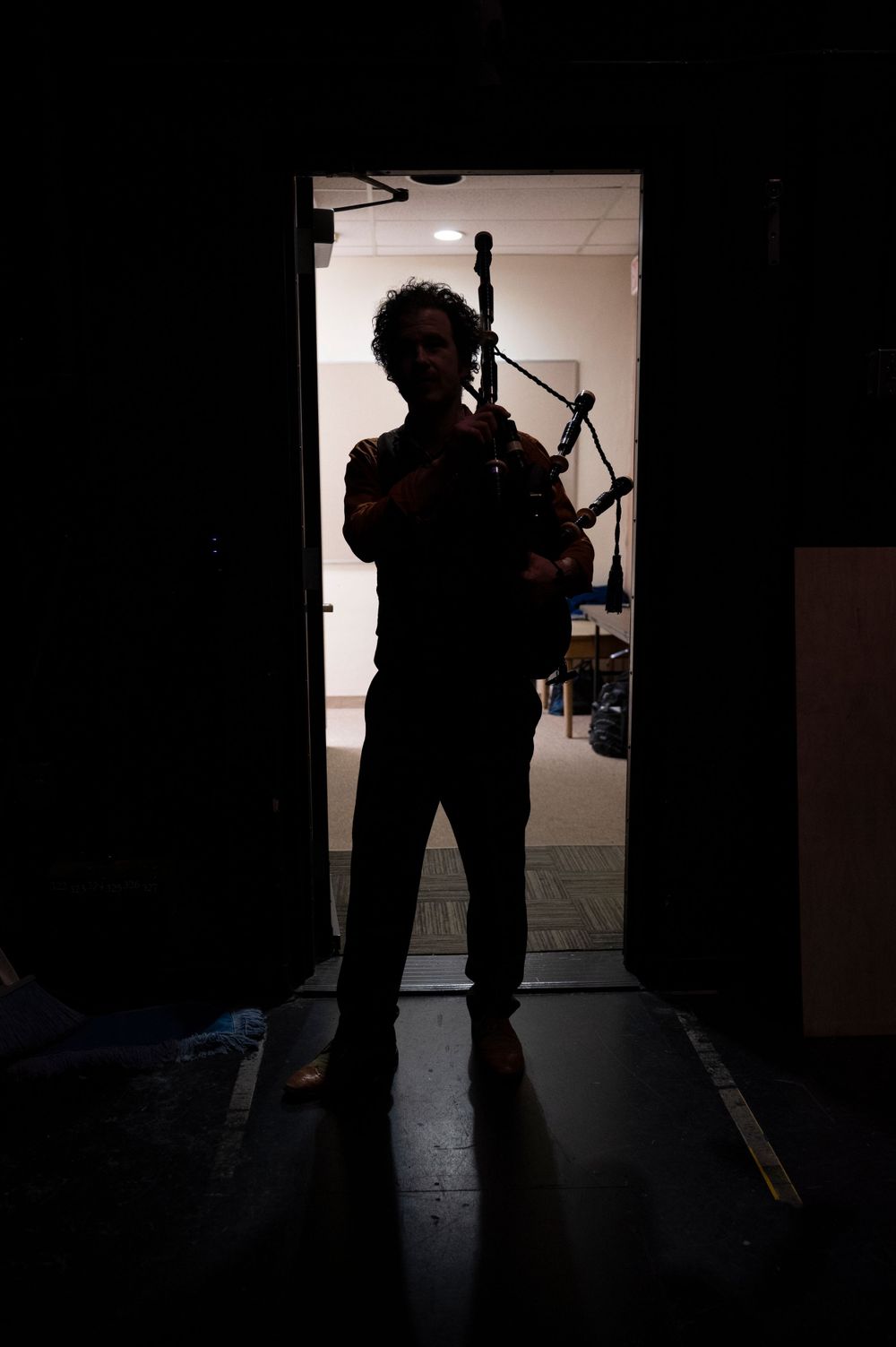 Silhouette of bagpiper performing in doorway with dramatic lighting.
