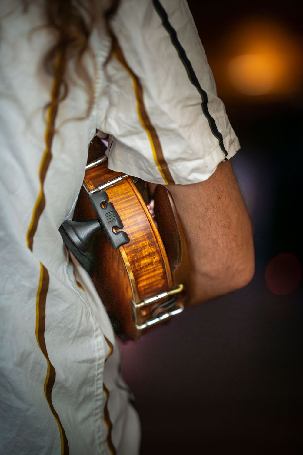 Close-up detail shot of acoustic guitar body and player's white sleeve in warm lighting.