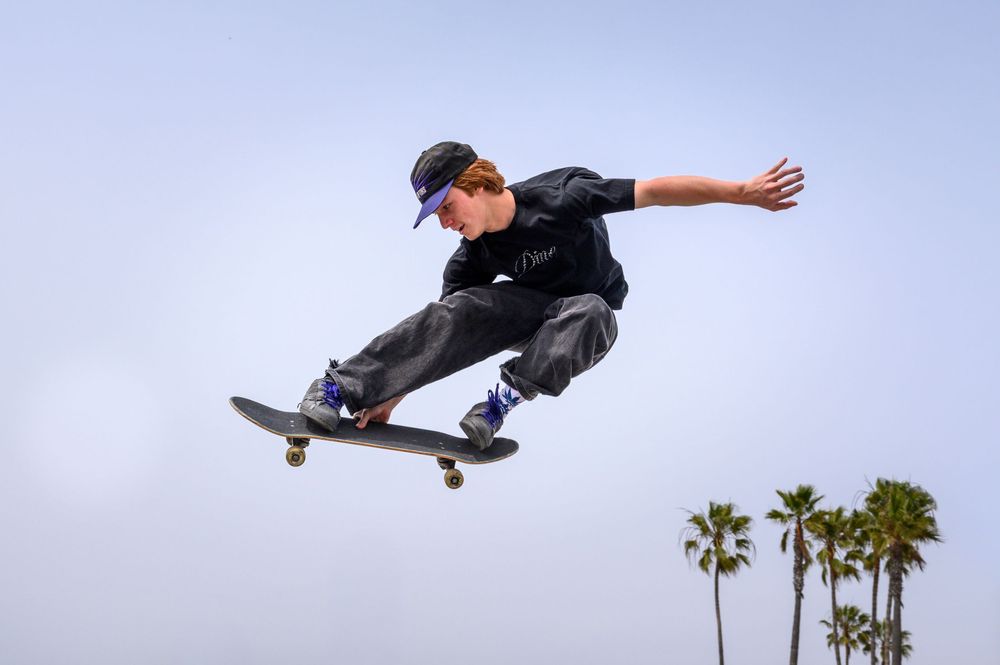 Young skateboarder performing an aerial trick with palm trees in the background against a clear sky.